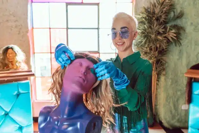 Woman styling a curly wig on a mannequin, demonstrating proper wig maintenance