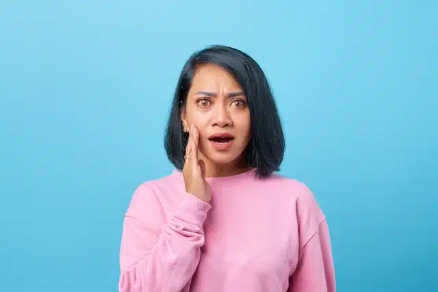Woman holding her cheek in pain, showing signs of a sudden toothache