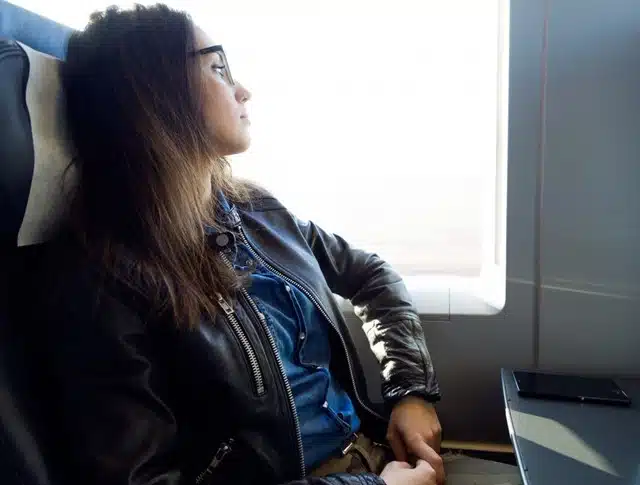 A woman in a leather jacket gazing out the window while seated on a plane during travel