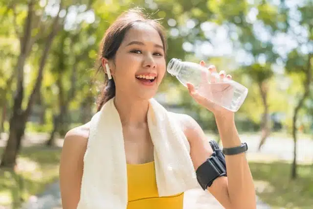 A young woman drinking water outdoors after a workout to support post-travel recovery and hydration