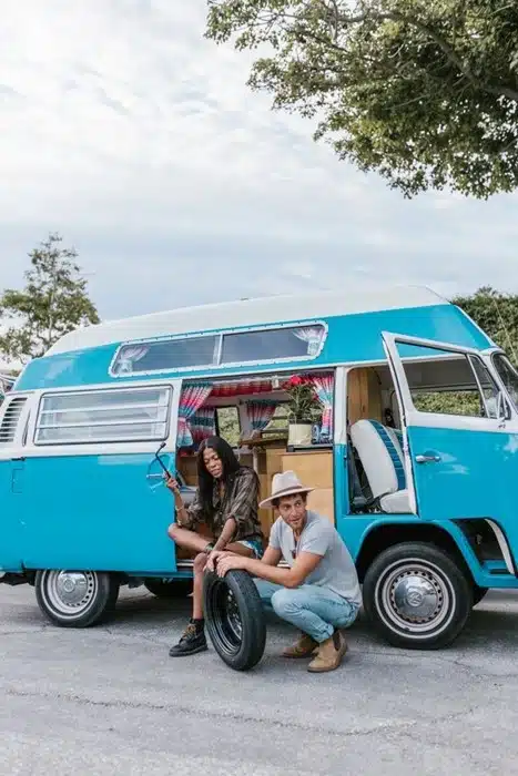 Couple checking a spare trailer tires for luxury camping trip beside their campervan