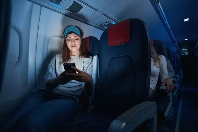 Woman playing an offline game on her phone during a flight, sleep mask on her forehead in a dimly lit cabin