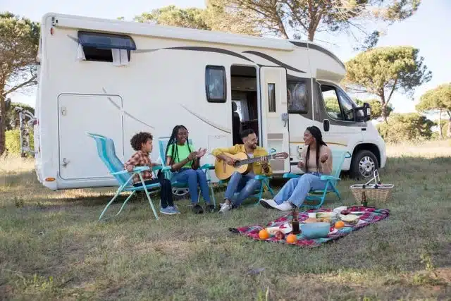 Family enjoying a picnic and music beside their glamping trailer