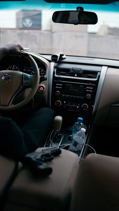 A driver's view inside a car with a handgun placed on the seat, highlighting proper firearm storage while traveling on the road