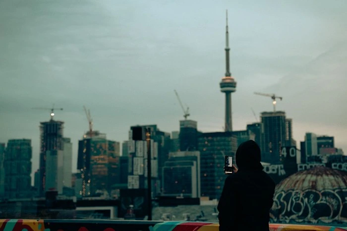 Tourist using mobile data on phone with Toronto skyline and CN Tower in background