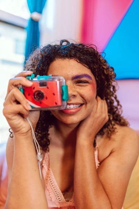 Woman holding a fun watermelon-print camera, a playful example of personalized creator gear