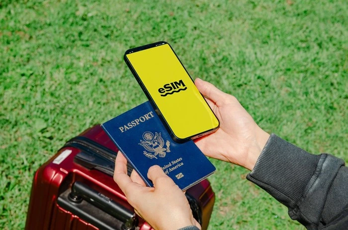 Traveler holding passport and phone with eSIM app near red suitcase for Canada trip