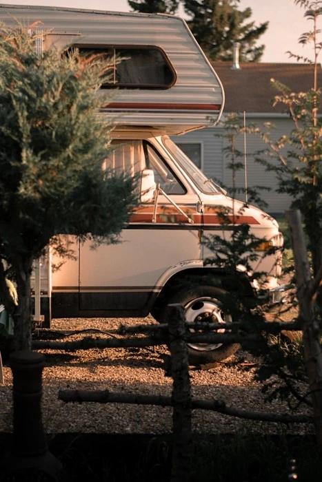 RV travel benefits captured in this classic camper van parked beside a house, framed by trees at golden hour