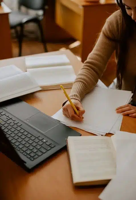 Student handwriting notes with laptop and open books, online learning discipline