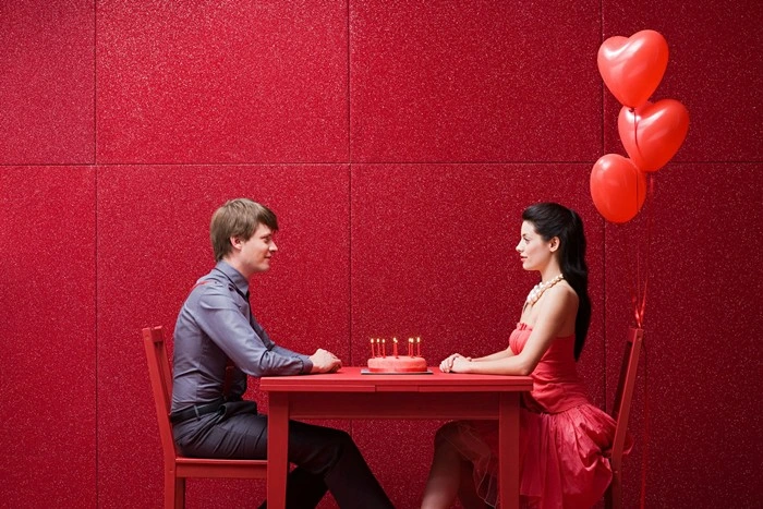Man and woman on a date at a red-themed table with heart balloons