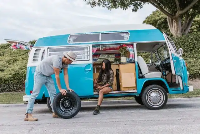 Man rolling a spare tire toward his trailer for a luxury camping getaway