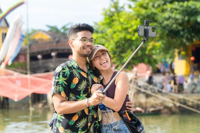 Content creator couple using a selfie stick to film travel content by a riverside market