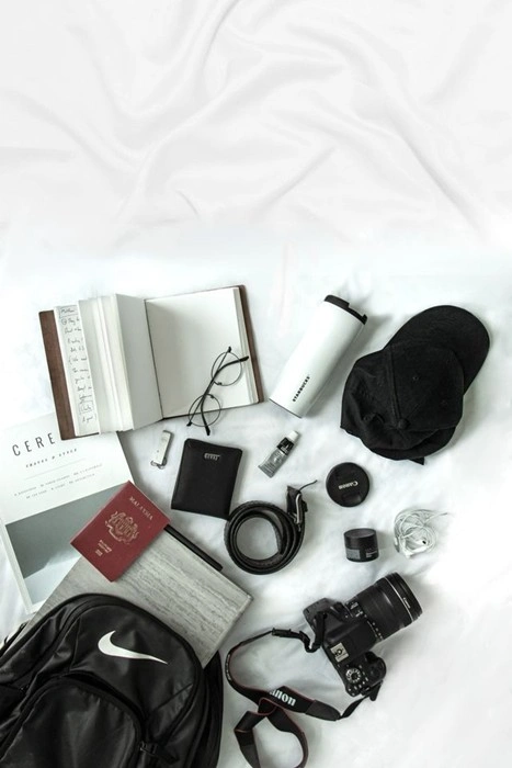 Travel gear for content creators laid out flat, including a Canon camera, backpack, passport, and notebook