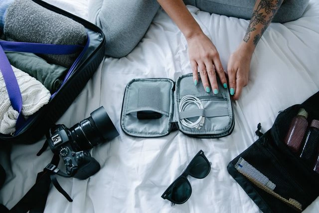 Tech organizer pouch with cables, camera, and sunglasses packed for travel