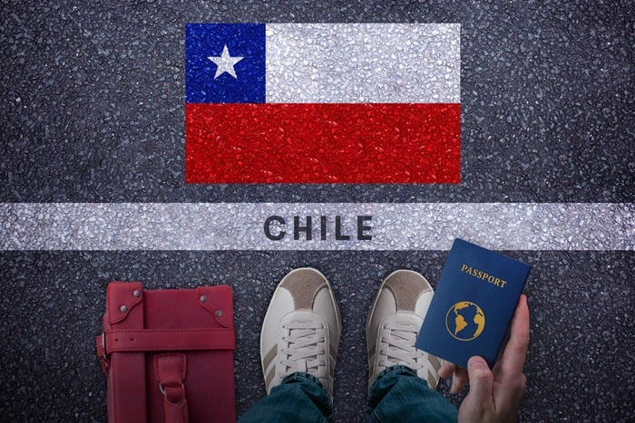 Passport, red bag, and shoes standing beside a Chilean flag painted on the ground, symbolizing an upcoming trip to Chile