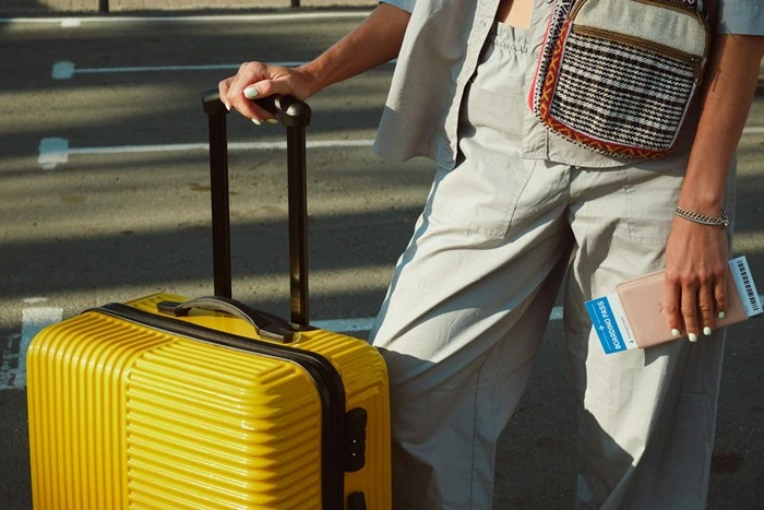 A traveler holding a yellow suitcase and boarding pass, ready for a trip while carrying a concealed carry purse