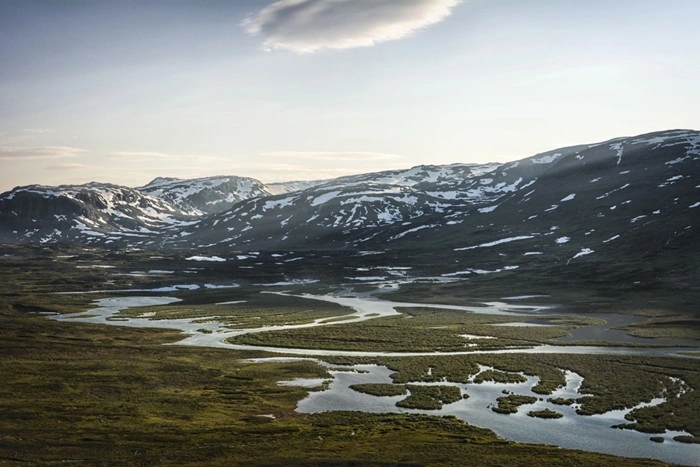 Tundra landscape in Lapland with winding rivers and patches of melting snow across the hills