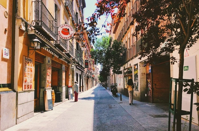 Sunlit street lined with restaurants and shops in a quiet Madrid neighborhood