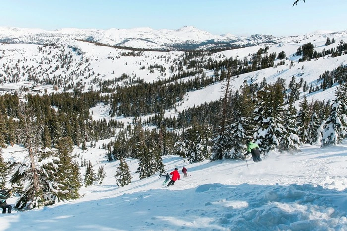Skiers descending a wide mountain bowl with panoramic views at Kirkwood