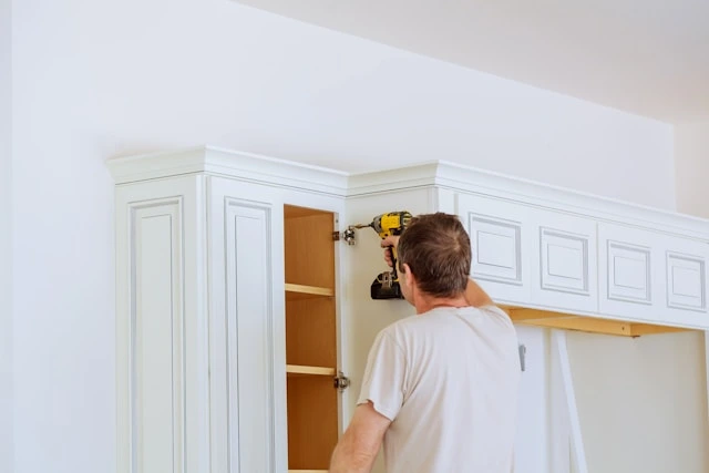 Handyman drilling white kitchen cabinet hinge during a remodeling installation
