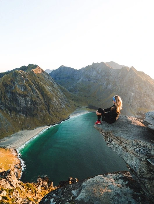 Woman sitting on cliff edge overlooking mountains and turquoise bay, showing the benefits of adventure travel