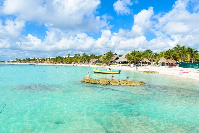 Riviera Maya beach near Cancun with calm turquoise waters, palm-lined shore, and traditional boat