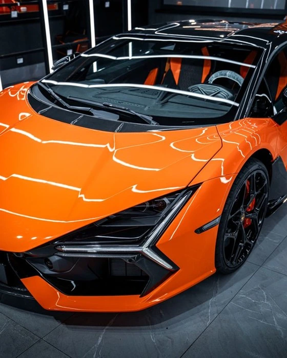 Glossy orange supercar with a cast vinyl wrap and white racing stripe accents, parked in a Dubai detailing studio