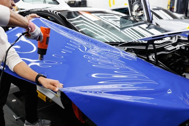 Technician using a heat gun during car wrapping in Dubai to install blue vinyl film on a car hood