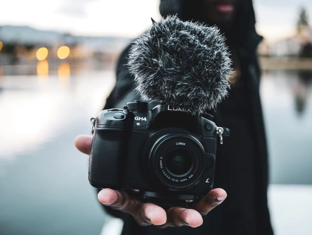 Creator holding a Panasonic Lumix GH4 camera with furry microphone for AI travel video