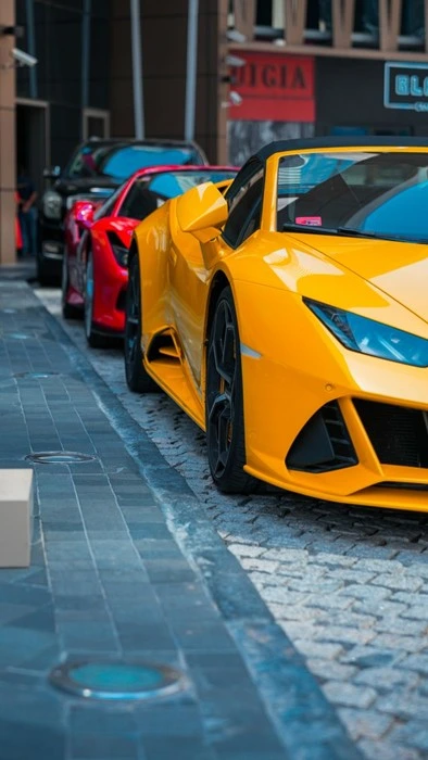 Row of yellow, red, and black wrapped luxury sports cars parked on a Dubai street