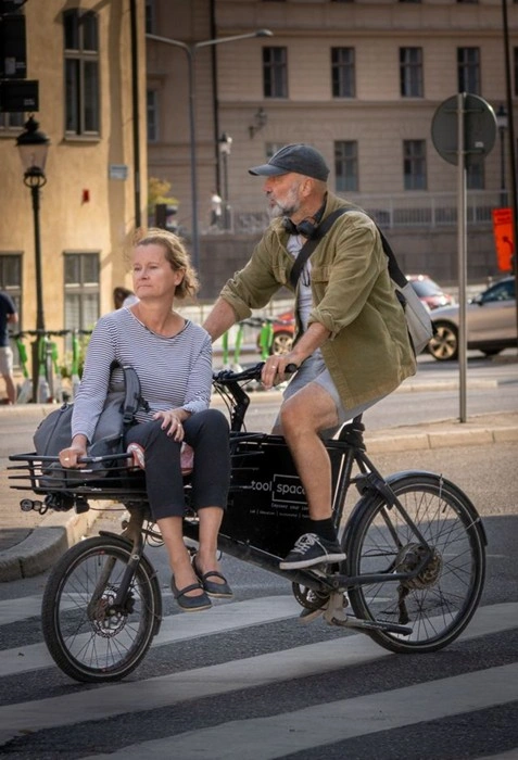 Man riding a cargo e-bike with a passenger seated in the front cargo area