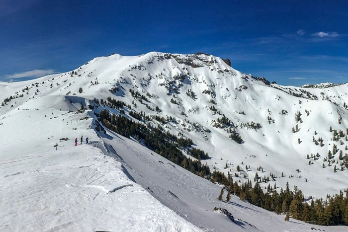 Things to do in Kirkwood Mountain Resort California — skiers on a snowy ridge with mountain peaks in the background