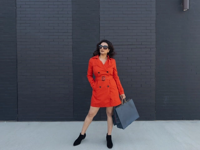 Woman styling a casual belted trench dress with black boots and a tote against a brick wall