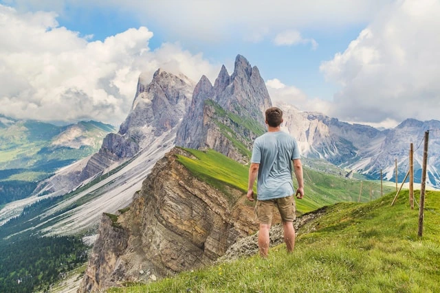 Man in comfortable travel clothing standing on a mountain ridge overlooking dramatic peaks