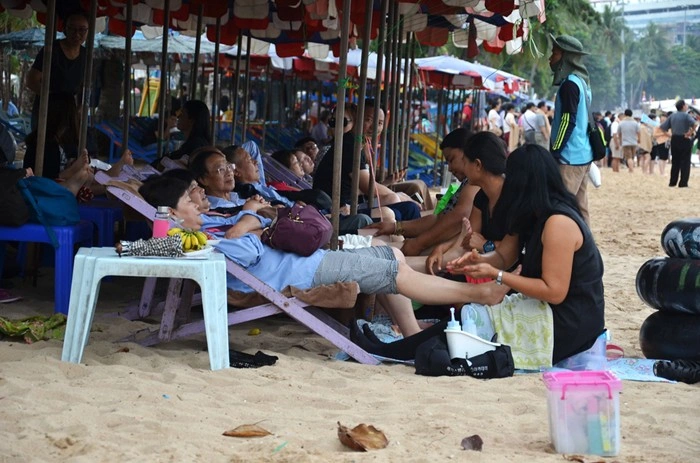 Traditional Thai massage on the beach in Pattaya, with visitors relaxing under sun umbrellas