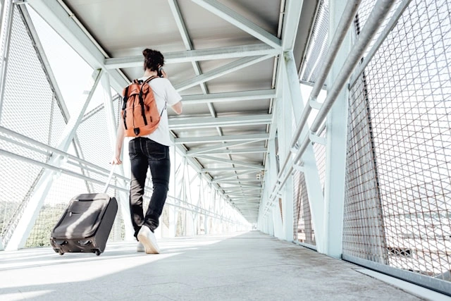 Stylish male traveler walking through an airport corridor with a backpack and rolling luggage
