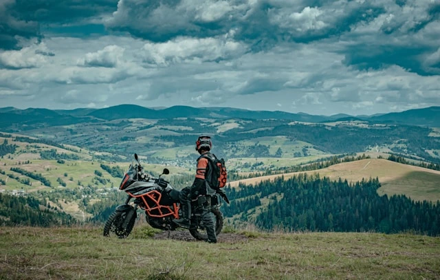 Rider taking in sweeping green hills and valleys beside an adventure motorbike under a cloudy sky