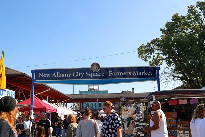 New Albany City Square Farmers Market sign with visitors browsing local vendor stalls