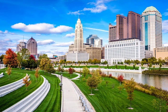 Columbus skyline overlooking the Scioto Mile riverfront park with green lawns, walking paths, and downtown buildings.