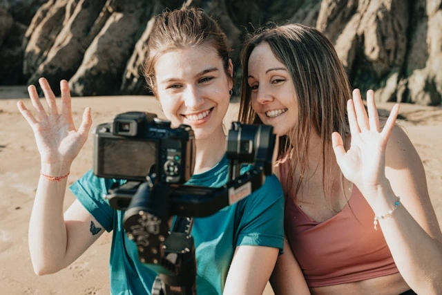 Two travel content creators waving on camera at a beach