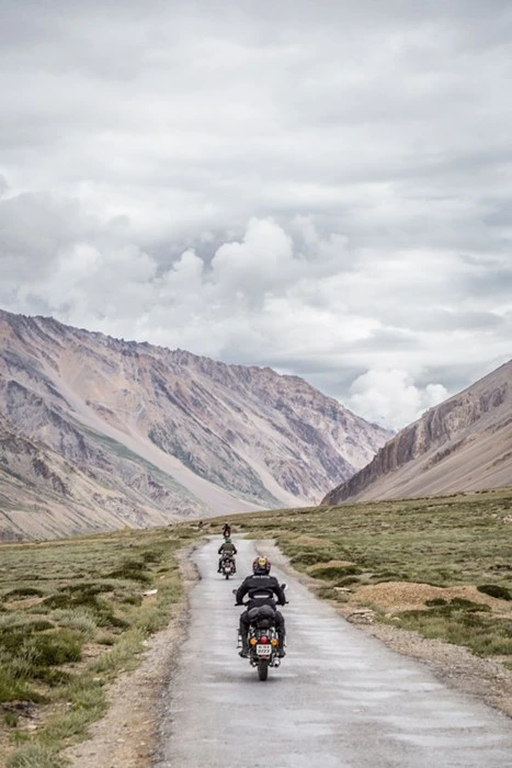 Motorbikes riding down a remote mountain valley road flanked by rugged peaks