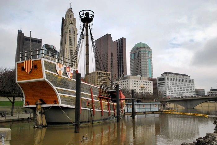 Replica ship along the Scioto River with the Columbus skyline and downtown bridges in the background.