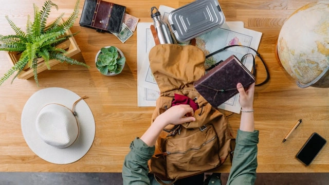 Traveler packing a backpack with reusable bottle, map, and travel essentials