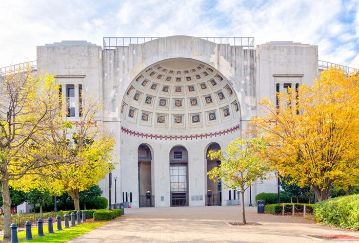 Rotunda entrance at Ohio Stadium in Columbus, framed by autumn trees and a paved walkway.