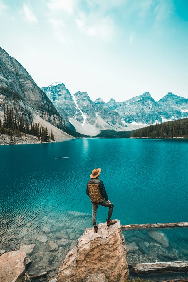 Stylish tips for men travelers — man in a layered vest and hat overlooking a turquoise mountain lake
