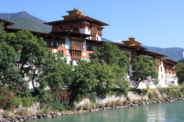 Traditional Bhutanese dzong overlooking a river surrounded by mountains and greenery