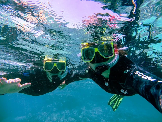 Two travelers wearing scuba masks and gear underwater, trying a new adventure activity together