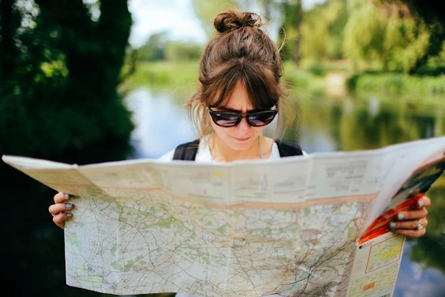 Woman with backpack reading a map outdoors while traveling solo
