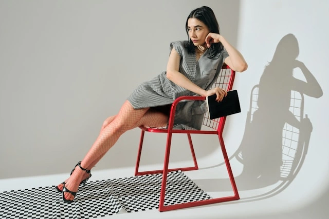 Woman in a checkered dress and heels sitting on a red chair for a stylish women's work outfit look