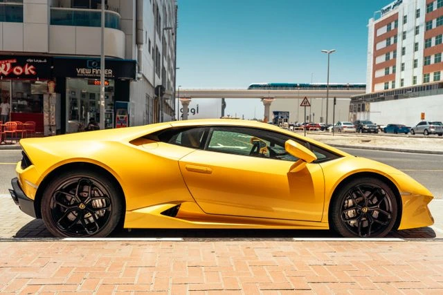 Matte gold wrapped Lamborghini parked on a Dubai street with the metro line in the background